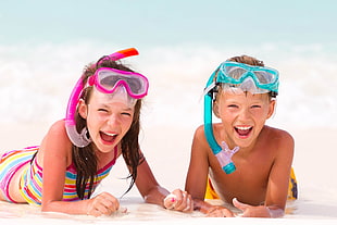 girl and boy wearing snorkels while stomach lying on white sand
